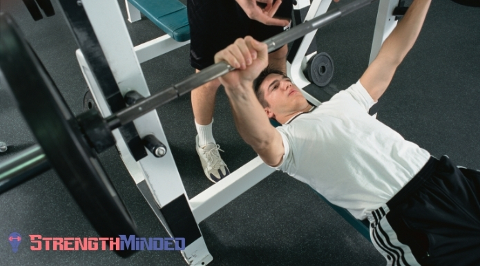 spotter helping man with bench press exercise